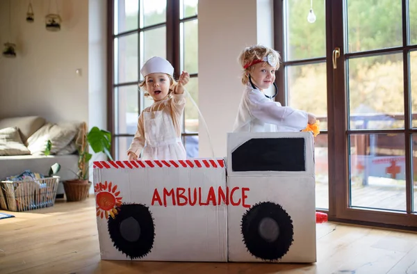 Duas crianças pequenas com uniformes médicos dentro de casa, brincando . — Fotografia de Stock