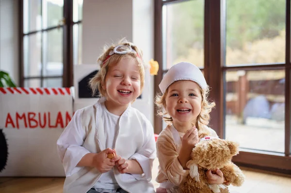 Dvě malé děti s lékařskými uniformami doma, hrající si. — Stock fotografie