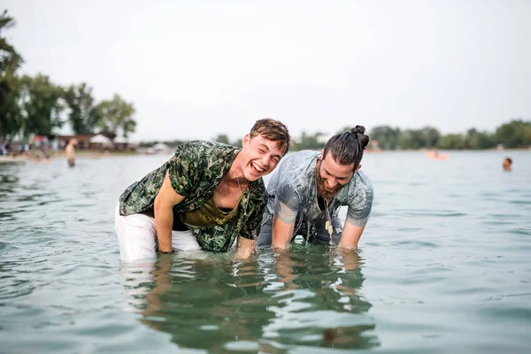 Mokří mladí muži přátelé na letním festivalu, stojící v jezeře. — Stock fotografie