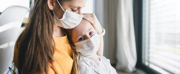 Moeder en kind met gezichtsmaskers binnenshuis, Corona virus en quarantaine concept. — Stockfoto