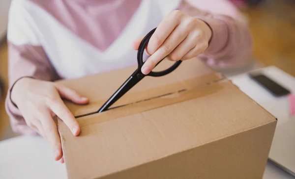 Mujer joven irreconocible en la mesa, abriendo la caja de paquetes . — Foto de Stock