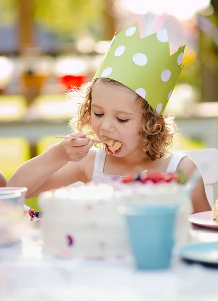 Petite fille assise à l'extérieur dans le jardin en été, manger du gâteau . — Photo