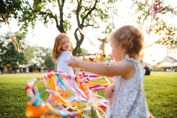 Kleine meisjes buiten in de tuin in de zomer, spelen met regenboog hand vlieger. — Stockfoto