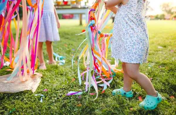 Невпізнавані маленькі дівчата на відкритому повітрі в саду влітку, грають з веселковим ручним змієм . — стокове фото