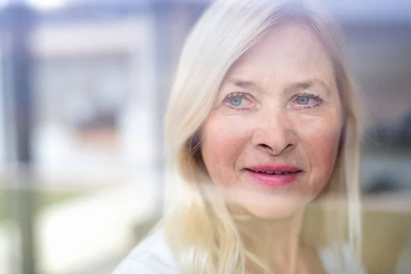 Porträt einer Seniorin, die zu Hause steht. Durch Glas geschossen. — Stockfoto