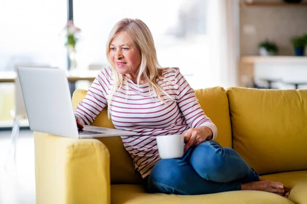 Mulher sênior com café e laptop em casa, relaxante . — Fotografia de Stock