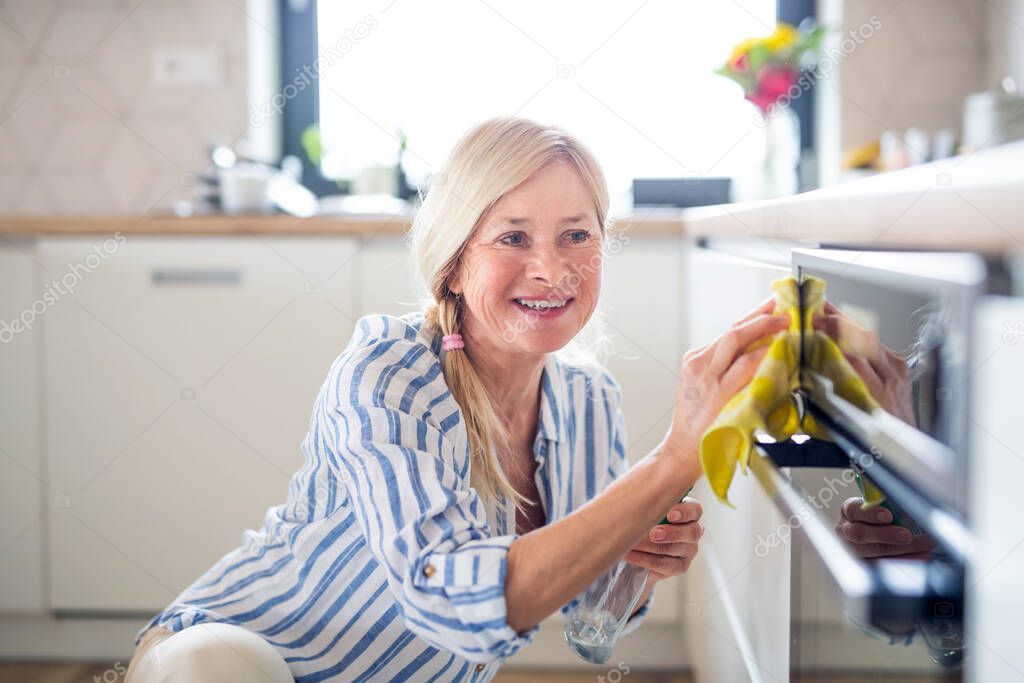 Portrait of senior woman cleaning oven door indoors in kitchen at home.