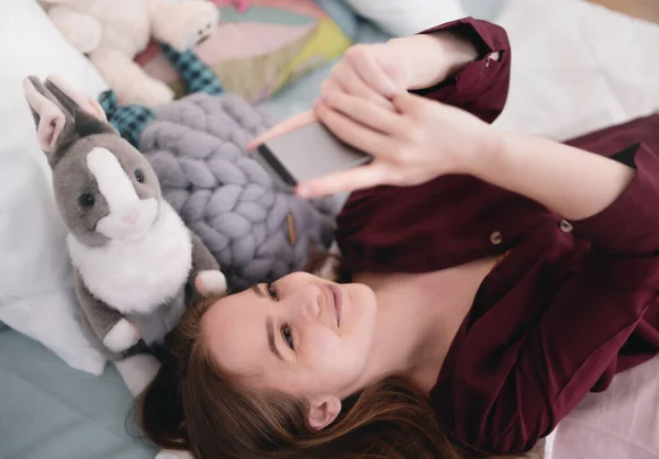 幸せな若い女の子の笑顔のトップビューとベッドの上で自撮り,オンラインデートのコンセプト. — ストック写真