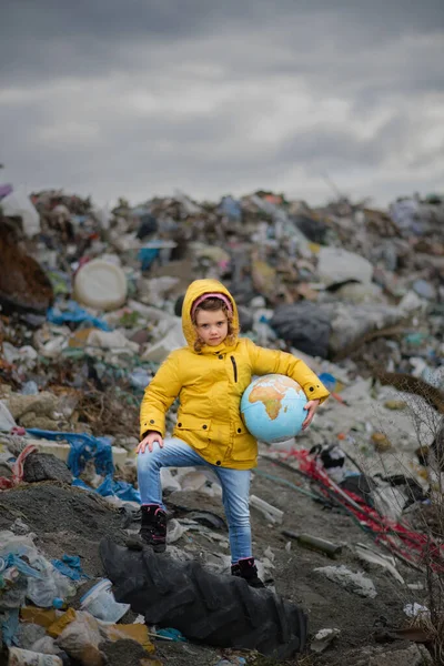 Arazi dolgusunda dünyayı tutan küçük bir çocuk, çevre kirliliği kavramı. — Stok fotoğraf