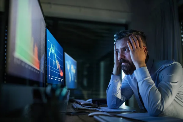 Empresário frustrado com computador sentado à secretária, a trabalhar até tarde. Conceito de crise financeira . — Fotografia de Stock