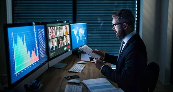 Um homem de negócios sério com um computador sentado à secretária, a trabalhar até tarde. Conceito de crise financeira . — Fotografia de Stock