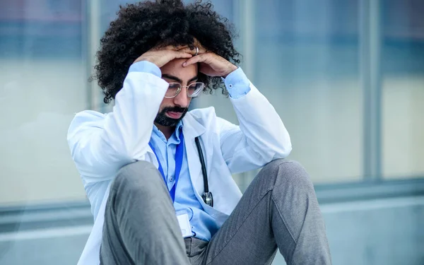 Znepokojený a unavený lékař sedí na podlaze v nemocnici, koncepce koronového viru. — Stock fotografie