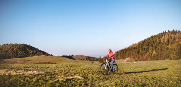 Actieve seniorenvrouw met e-bike fietsen in de natuur. — Stockfoto