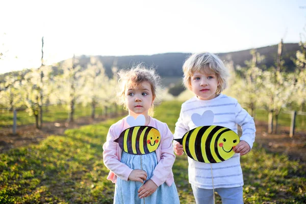 Zwei kleine Kinder stehen im Frühling draußen im Obstgarten mit Papierbienen. — Stockfoto