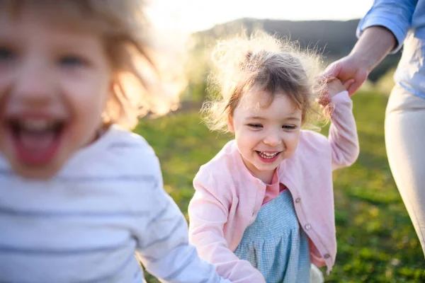 Duas crianças pequenas com a mãe correndo ao ar livre no pomar na primavera . — Fotografia de Stock