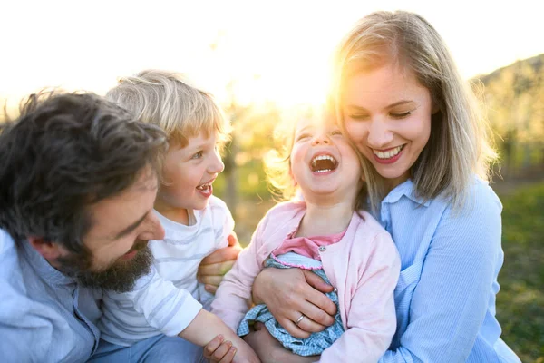 Familj med två små barn som skrattar utomhus i vårnaturen vid solnedgången. — Stockfoto