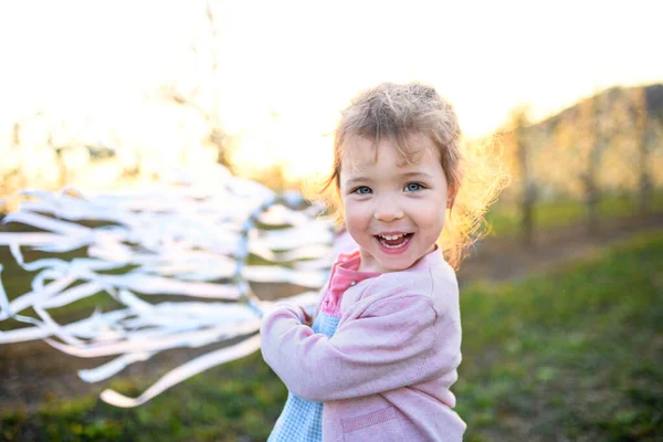 Menina pequena criança em pé ao ar livre no pomar na primavera, segurando anel de fita de mão . — Fotografia de Stock