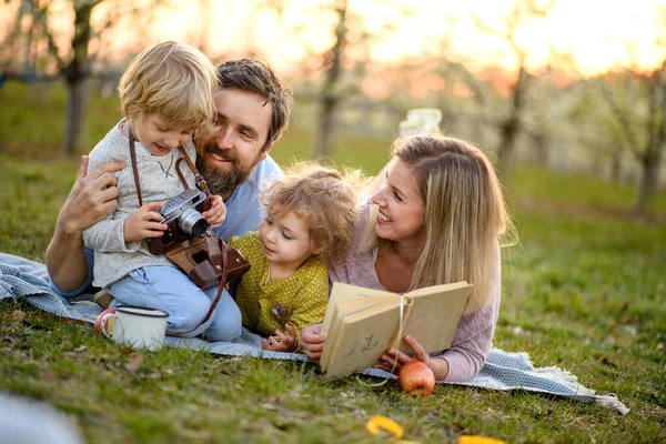 Familie en kleine kinderen met camera en boek buiten in de lente natuur, rusten. — Stockfoto
