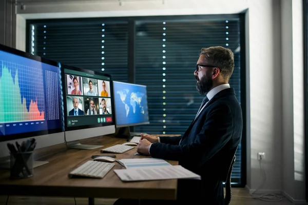 Un uomo d'affari serio con un computer seduto alla scrivania, che lavora fino a tardi. Business call concept . — Foto Stock