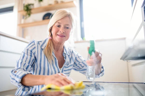 Portrait of senior woman cleaning oven door indoors in kitchen at home. — Stock Photo, Image