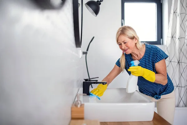 Femme âgée avec gants nettoyage salle de bains à l'intérieur à la maison . — Photo