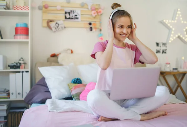 ベッドの上でヘッドフォンやラップトップを持つ若い女の子,隔離中にリラックス. — ストック写真