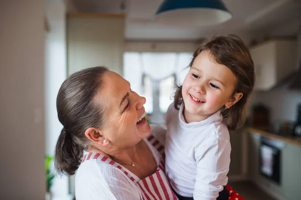 Small girl with senior grandmother in kitchen indoors at home. — Stock Photo, Image