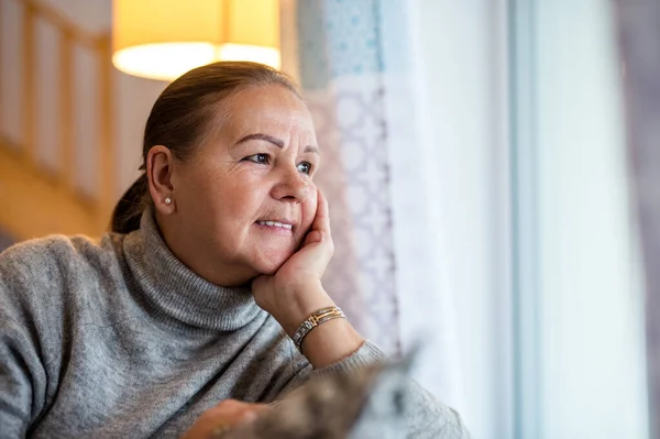 Närbild porträtt av äldre kvinna sitter vid fönstret inomhus. — Stockfoto