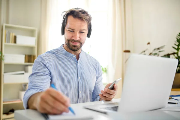 Érett üzletember fülhallgatóval és laptoppal az otthoni irodában, dolgozik. — Stock Fotó