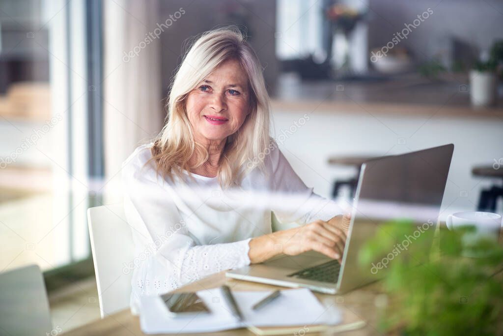 Senior woman with laptop indoors in home office, working.