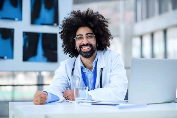 Portrét veselého mužského doktora sedícího v nemocnici, dívajícího se do kamery. — Stock fotografie