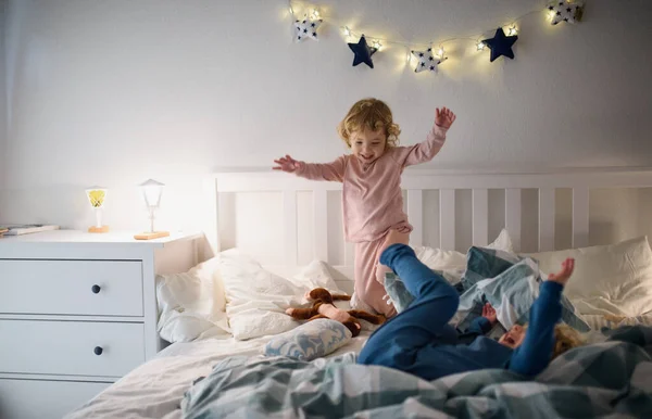 Duas crianças pequenas pulando na cama dentro de casa, se divertindo . — Fotografia de Stock