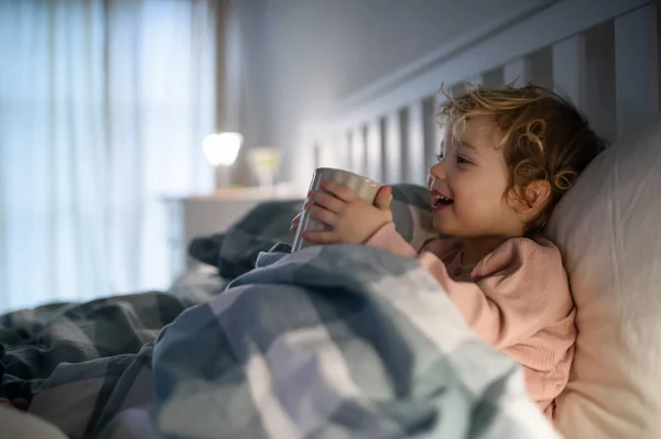 小さな病気の幼児の女の子は家の中でベッドの中に横たわって、カップを保持. — ストック写真