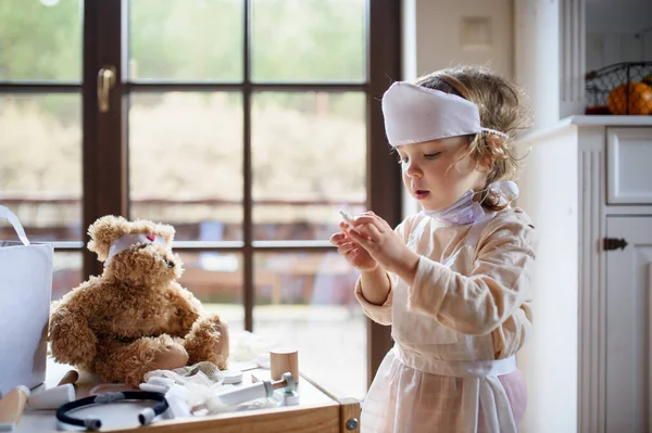 Klein peuter meisje met dokter uniform binnen, spelen. — Stockfoto