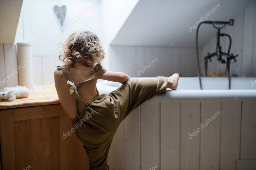 Rear view of small toddler child climbing into bath indoors at home.