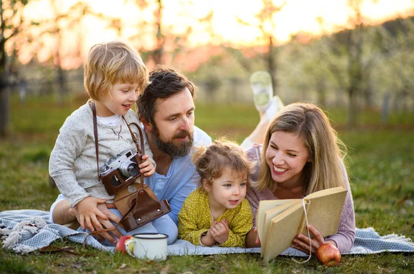 Familie en kleine kinderen met camera en boek buiten in de lente natuur, rusten. — Stockfoto