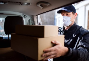 Yüzü maskeli kurye kasabaya paket kutusu getiriyor..