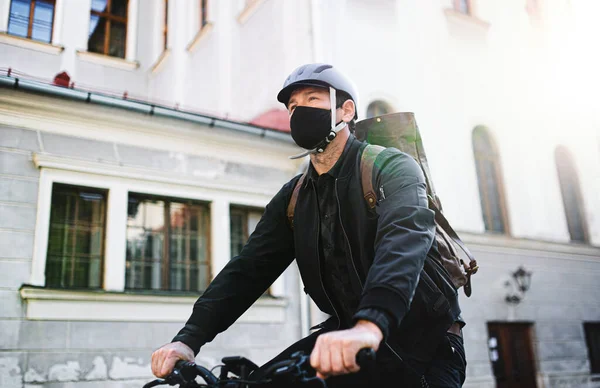 Entrega mensajero hombre con máscara facial y ciclismo en bicicleta en la ciudad . — Foto de Stock