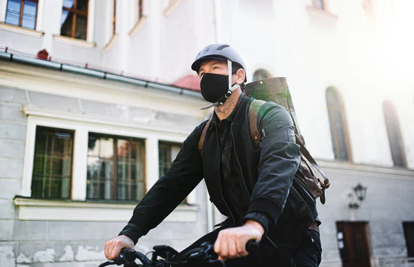 Entrega mensajero hombre con máscara facial y ciclismo en bicicleta en la ciudad . —  Fotos de Stock