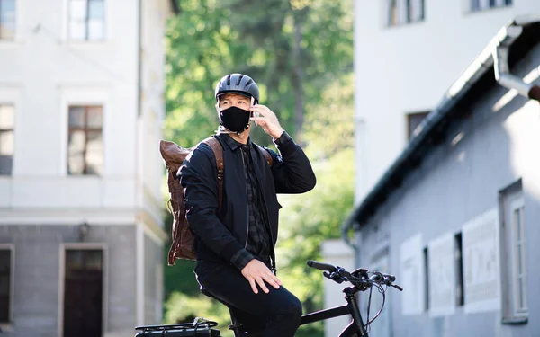 Entrega mensajero hombre con máscara facial y bicicleta usando smartphone en la ciudad . — Foto de Stock