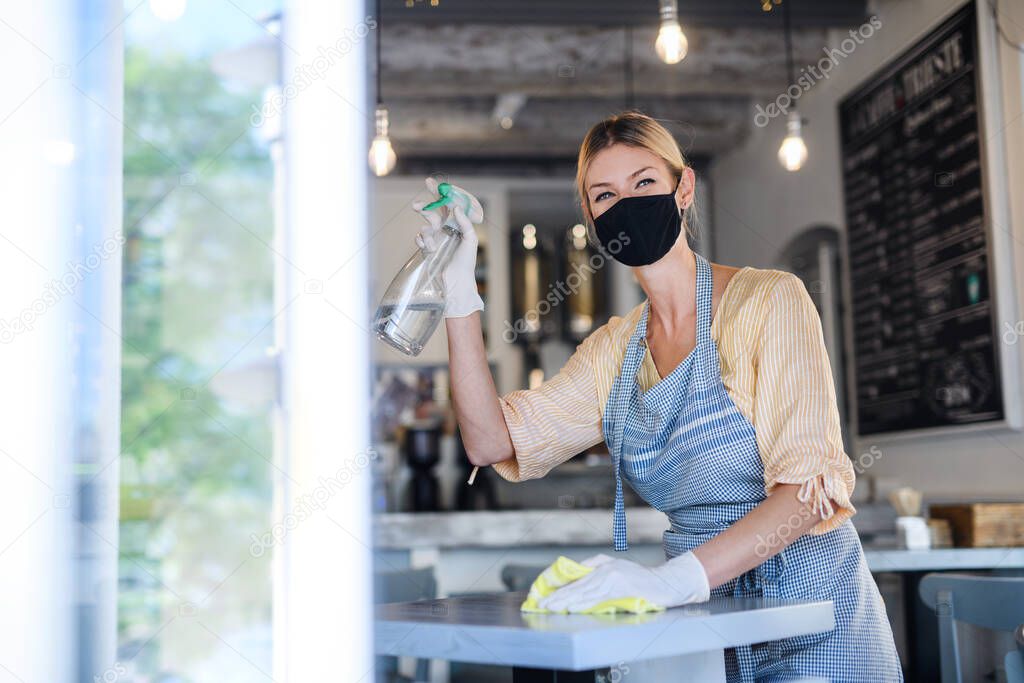 Coffee shop woman owner working with face mask and gloves , disinfecting tables.
