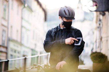 Kasabaya paket getiren yüz maskeli ve akıllı telefonlu kurye..