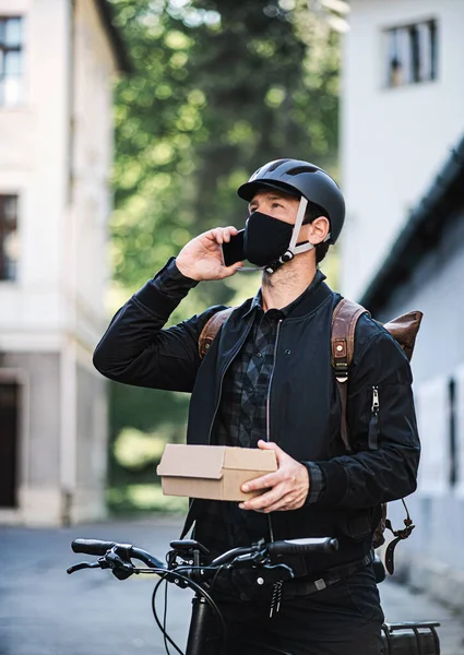 Entrega mensageiro homem com máscara facial e bicicleta usando smartphone na cidade . — Fotografia de Stock