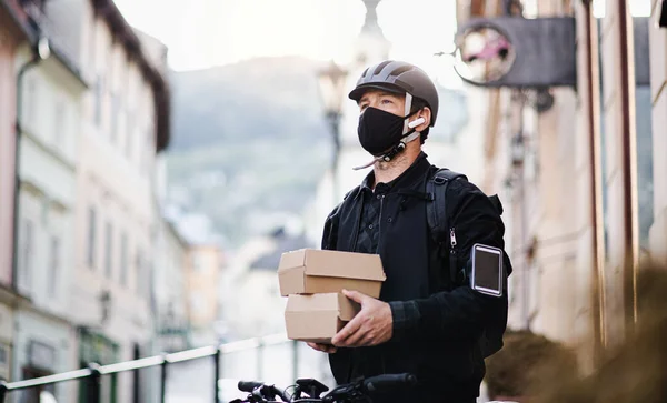 Futár arcmaszkkal és okostelefonnal csomagküldő doboz a városban. — Stock Fotó