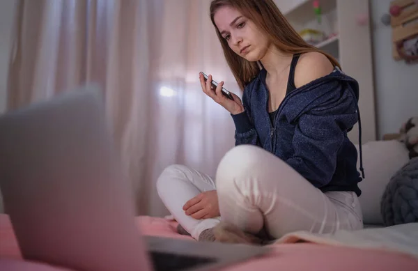 Bezorgd jong meisje met smartphone zittend binnen op bed, online dating concept. — Stockfoto