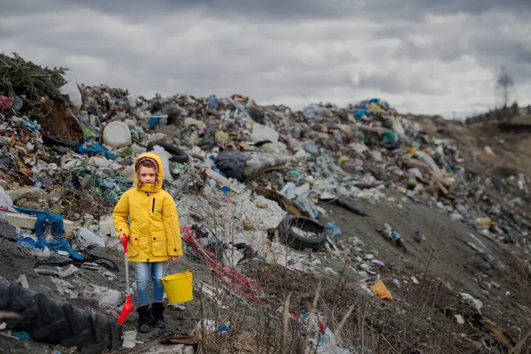 Arazi dolgusu üzerinde duran küçük bir çocuğun ön görünümü, çevre kirliliği kavramı. — Stok fotoğraf