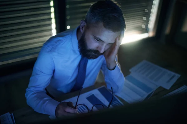 Empresário frustrado com computador sentado à secretária, a trabalhar até tarde. Conceito de crise financeira . — Fotografia de Stock