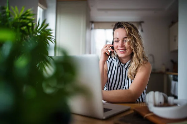 Jeune femme avec ordinateur portable et smartphone travaillant à l'intérieur à la maison . — Photo