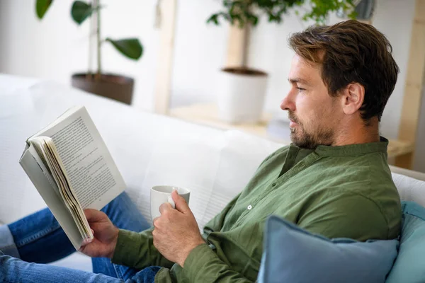 Чоловік сидить на дивані і читає книгу вдома, концепція блокування . — стокове фото
