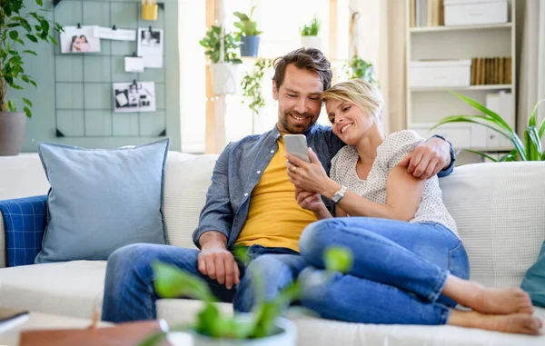 Pareja feliz en el amor sentado en el interior de casa, utilizando el teléfono inteligente . — Foto de Stock